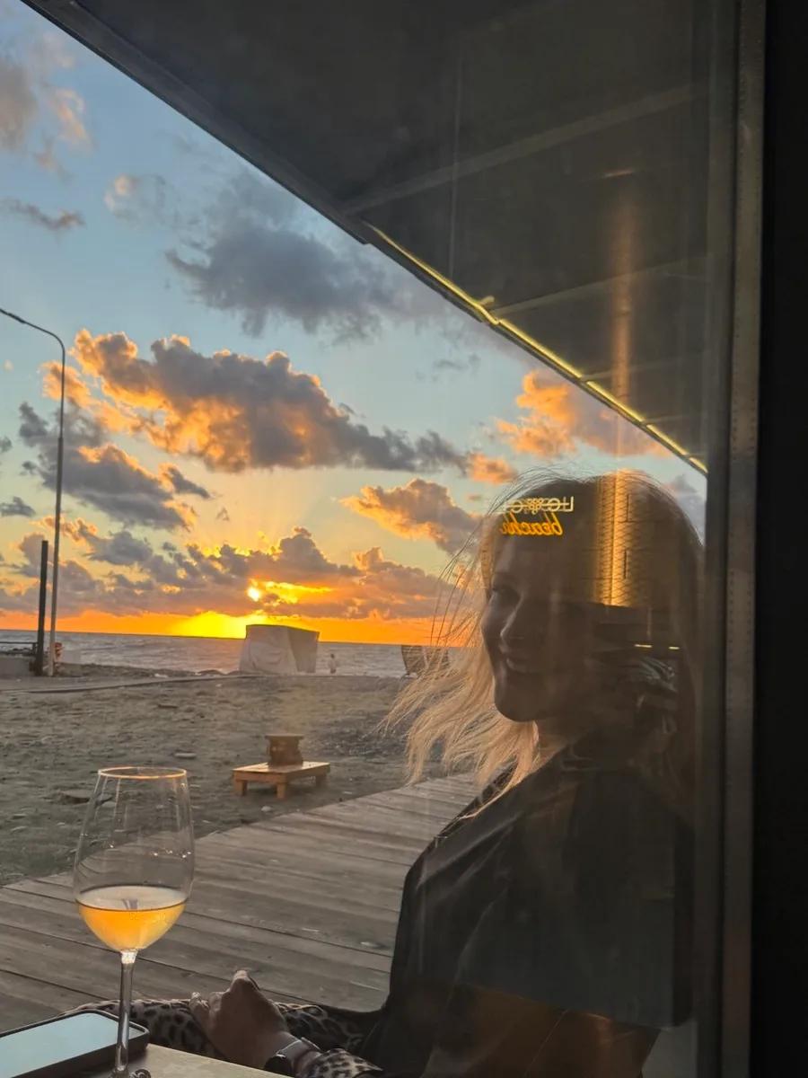 A smiling girl sits with a glass of white wine at sunset in LEVEL Beach Batumi
